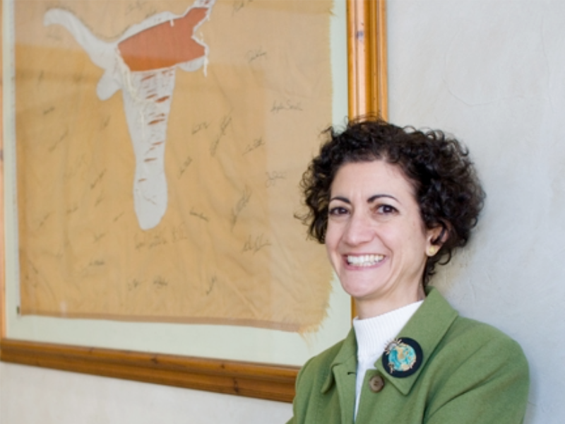 Alumna Lisa Guerra standing in front of UT Austin Longhorn framed flag.