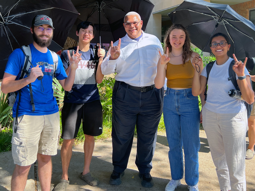 undergraduate students in student center making the hook 'em hand gesture and smiling