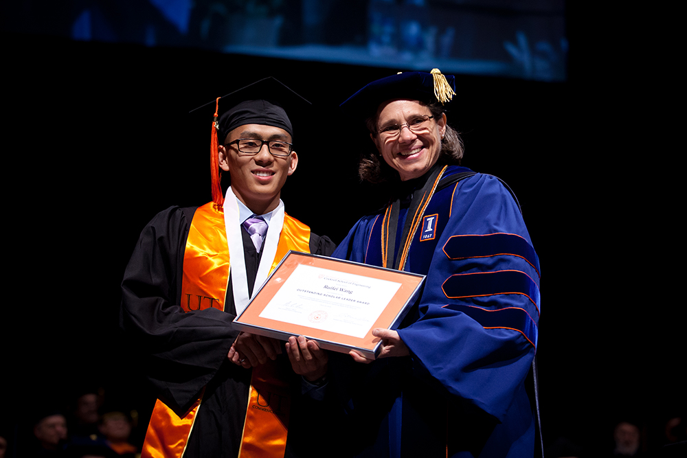Ruifei Wang holding award with Dean Sharon Wood onstage at graduation ceremony.