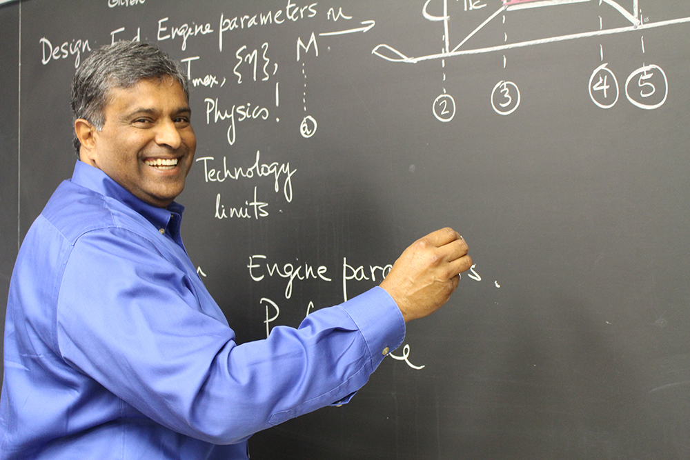 Philip Varghese smiling while writing at chalkboard.