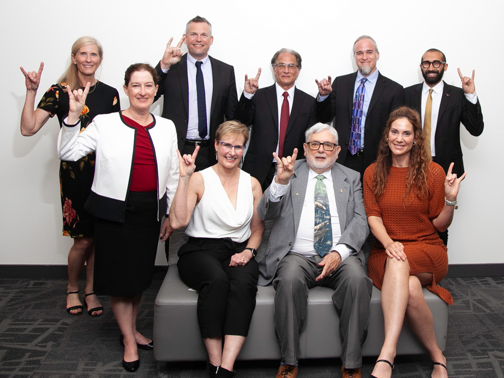 Group of Academy of Distinguished Alumni honorees sitting together and doing hook 'em horns hand sign.