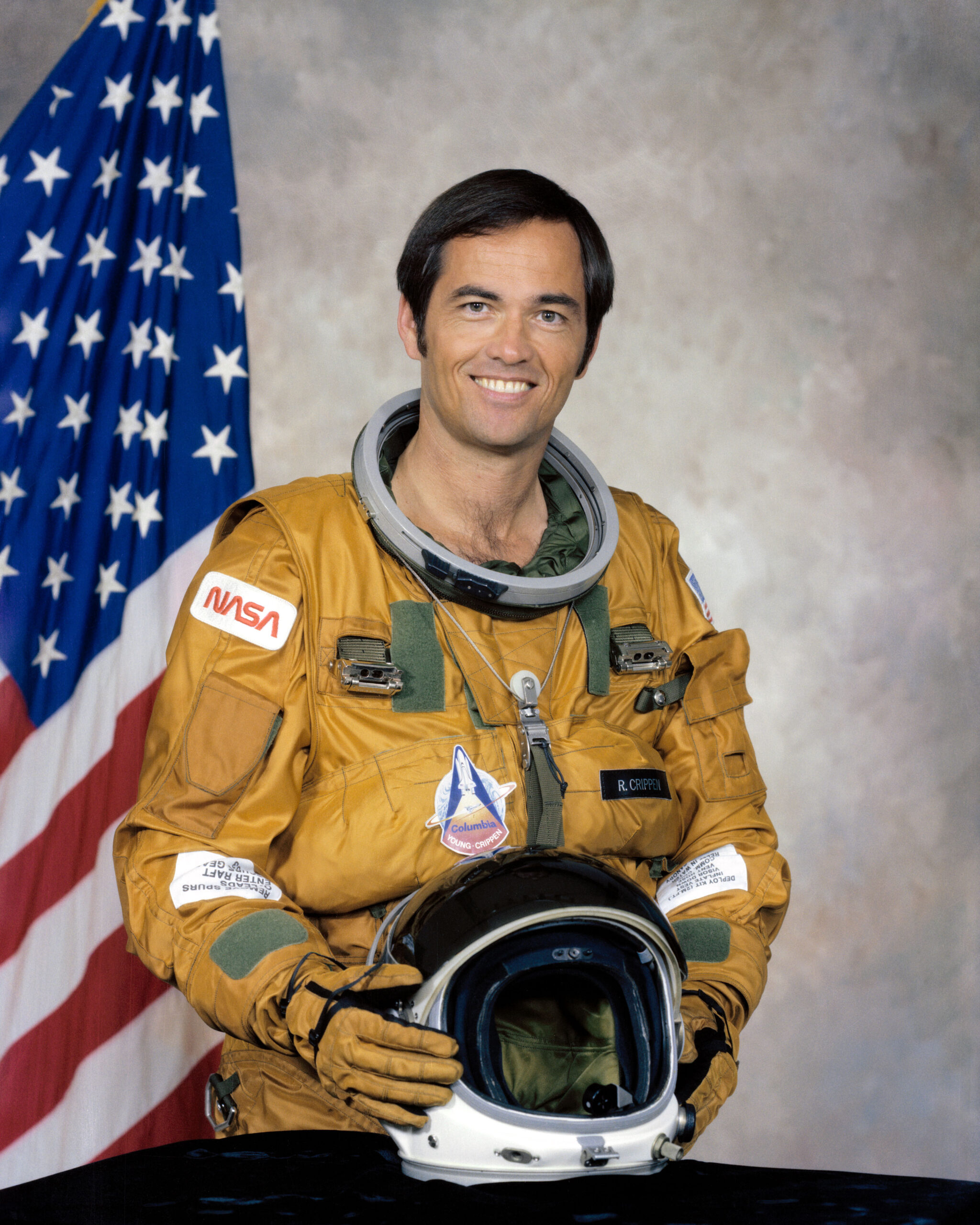 Alumnus Robert Crippen wearing spacesuit and holding helmet.