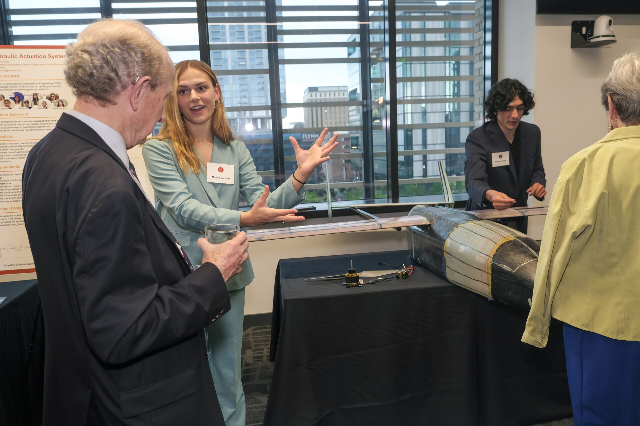 People present a UAV prototype to visitors at a professional event, with a project poster and city skyline in the background.