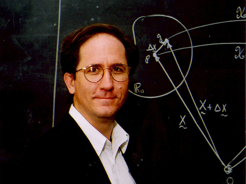 Texas Engineer Mark Mear standing in front of blackboard with equations written on it.