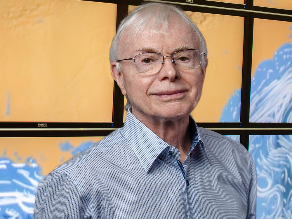 Thomas Hughes in front of large paneled visual screens in lab