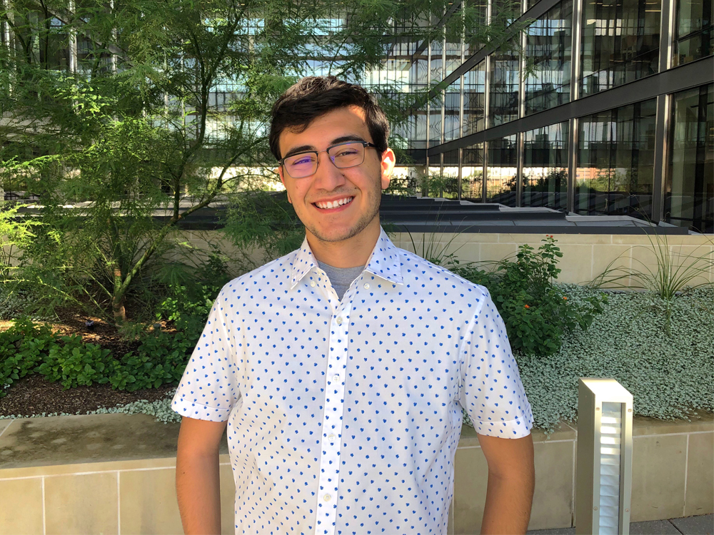Evan Silva smiling on UT Austin campus next to trees.