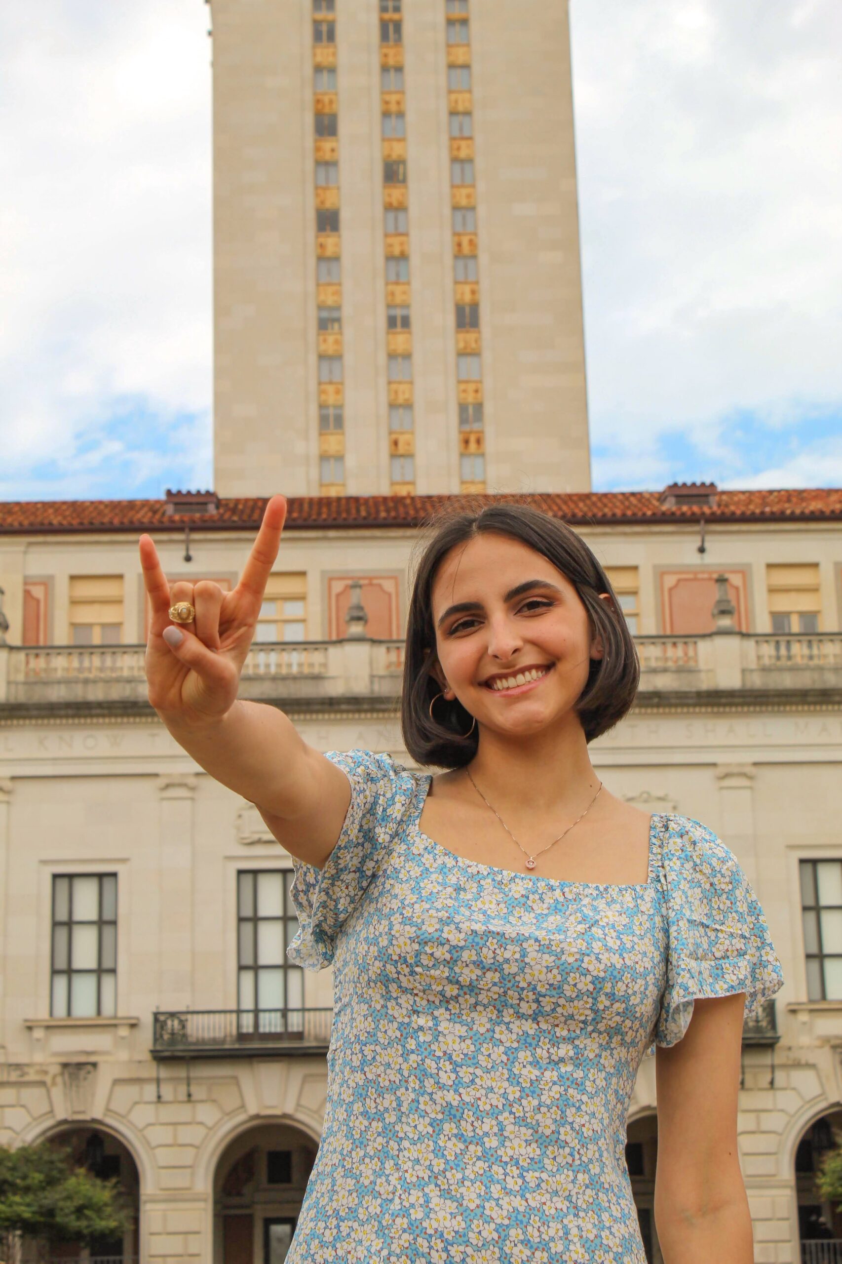 Azzurra Demarie doing a Hook 'em Horns hand sign in front of the UT Austin Tower