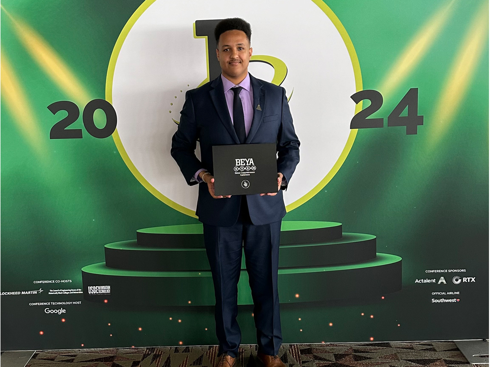Alumnus Nahum Alem holding award on podium.
