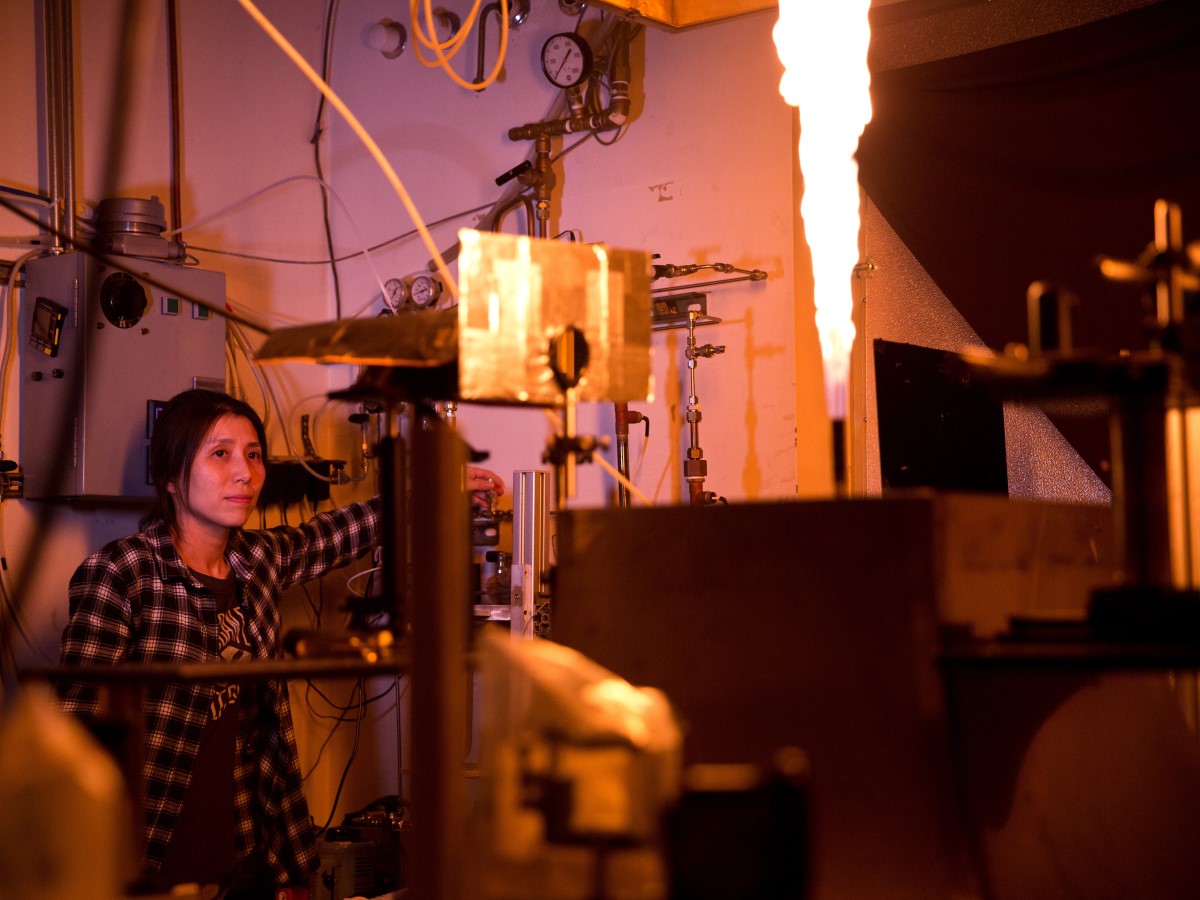 Researcher conducting experiments in combustion lab with flames coming out of pipe.