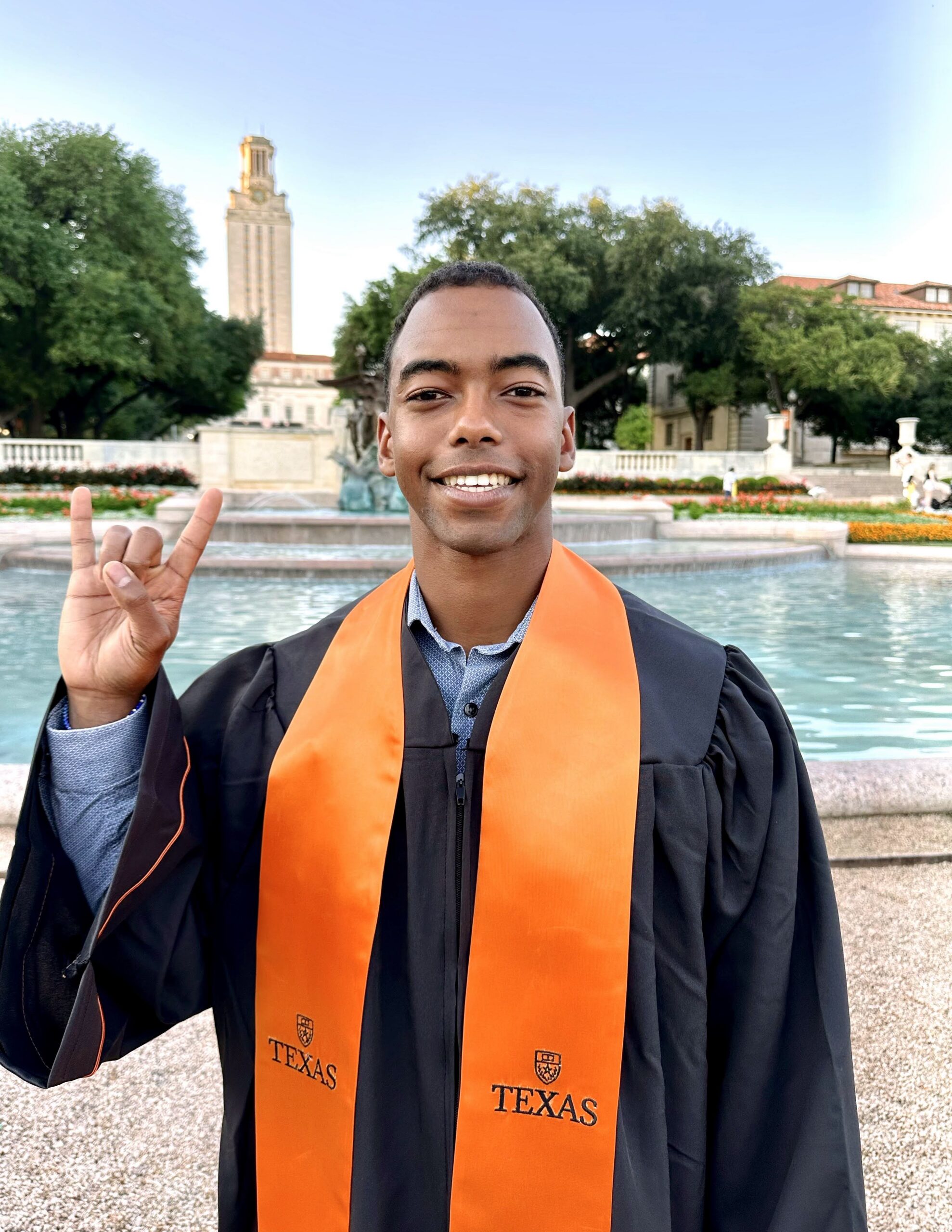 Texas Engineering student Taj Lee wearing graduation regalia and smiling in front of UT Tower