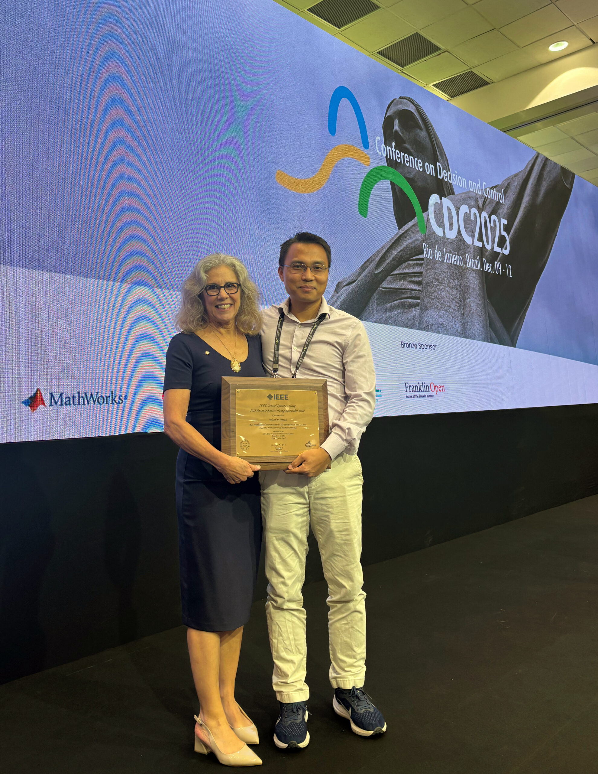 Thinh Doan standing onstage and holding award with advisor