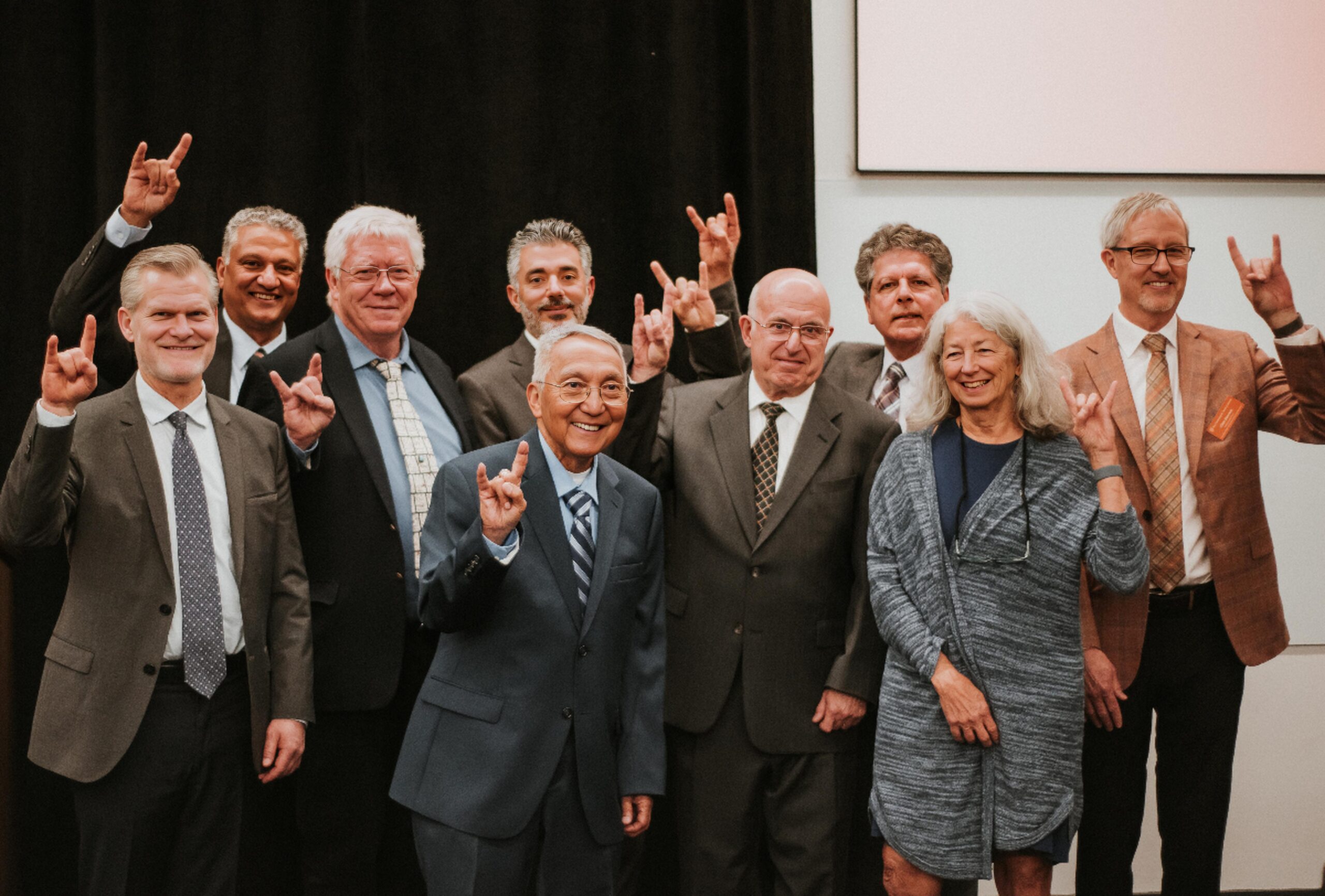 Group of Academy of Distinguished Alumni honorees smiling and doing hook 'em horns hand signs during 2025 awards banquet.