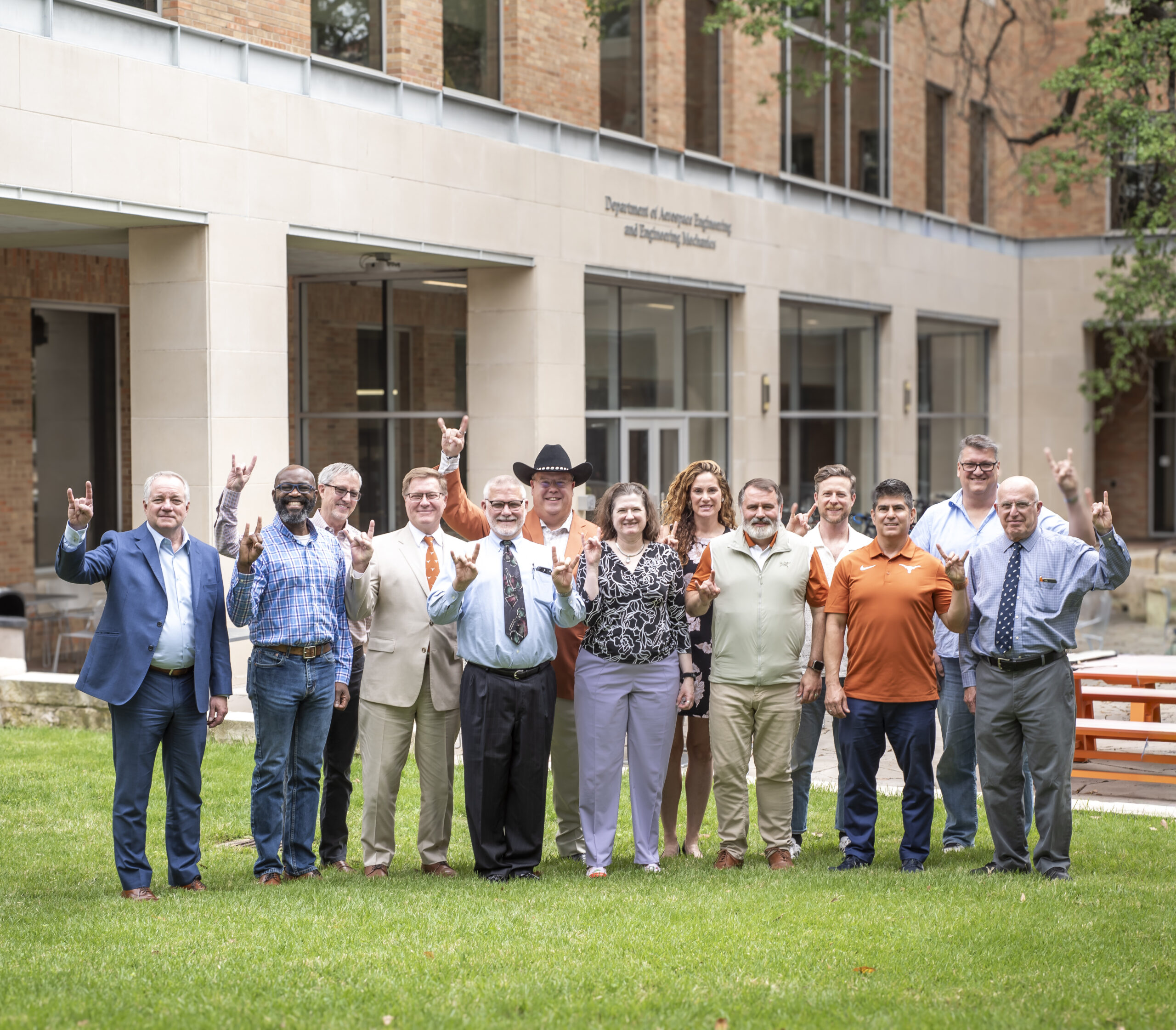 Group of ASE/EM's External Advisory Committee members gathered on UT Austin campus, smiling and doing hook 'em horns hand signs.