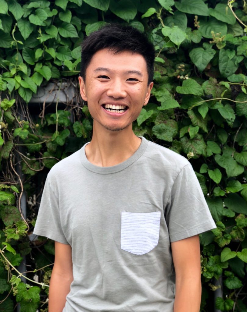 Max Li, assistant professor at the University of Michigan, smiling in front of large wall of greenery