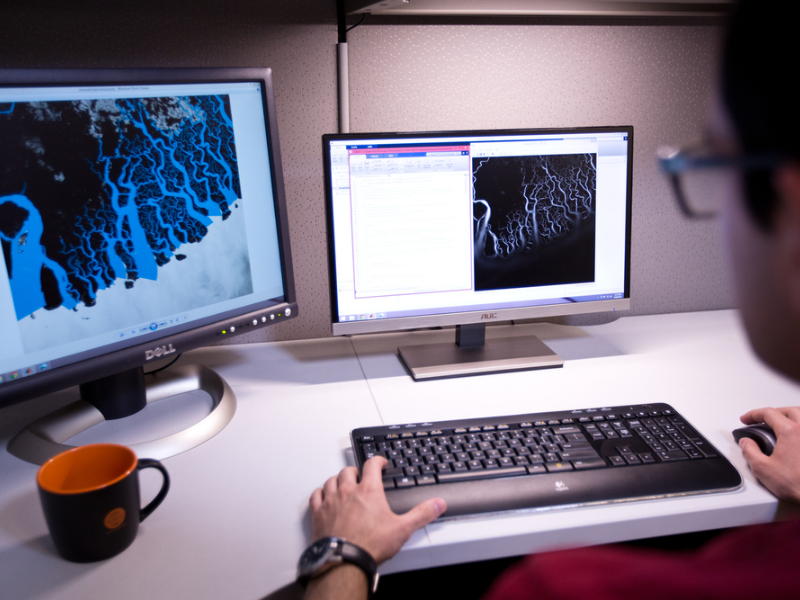 Person typing on computer keyboard with two monitors and a coffee cup on desk.