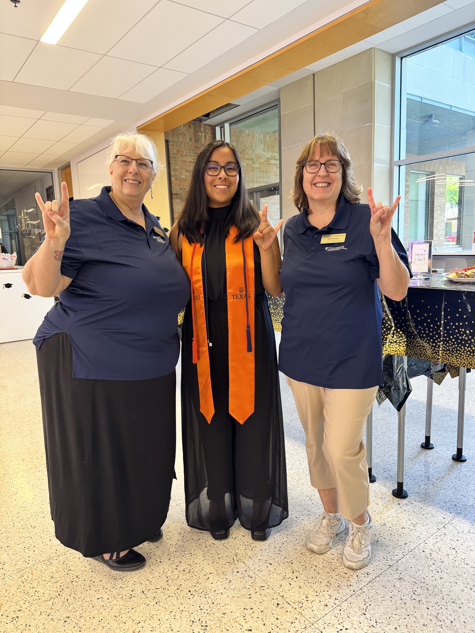 Holly Bhasin and Renee Babcock smiling with student wearing graduation regalia.