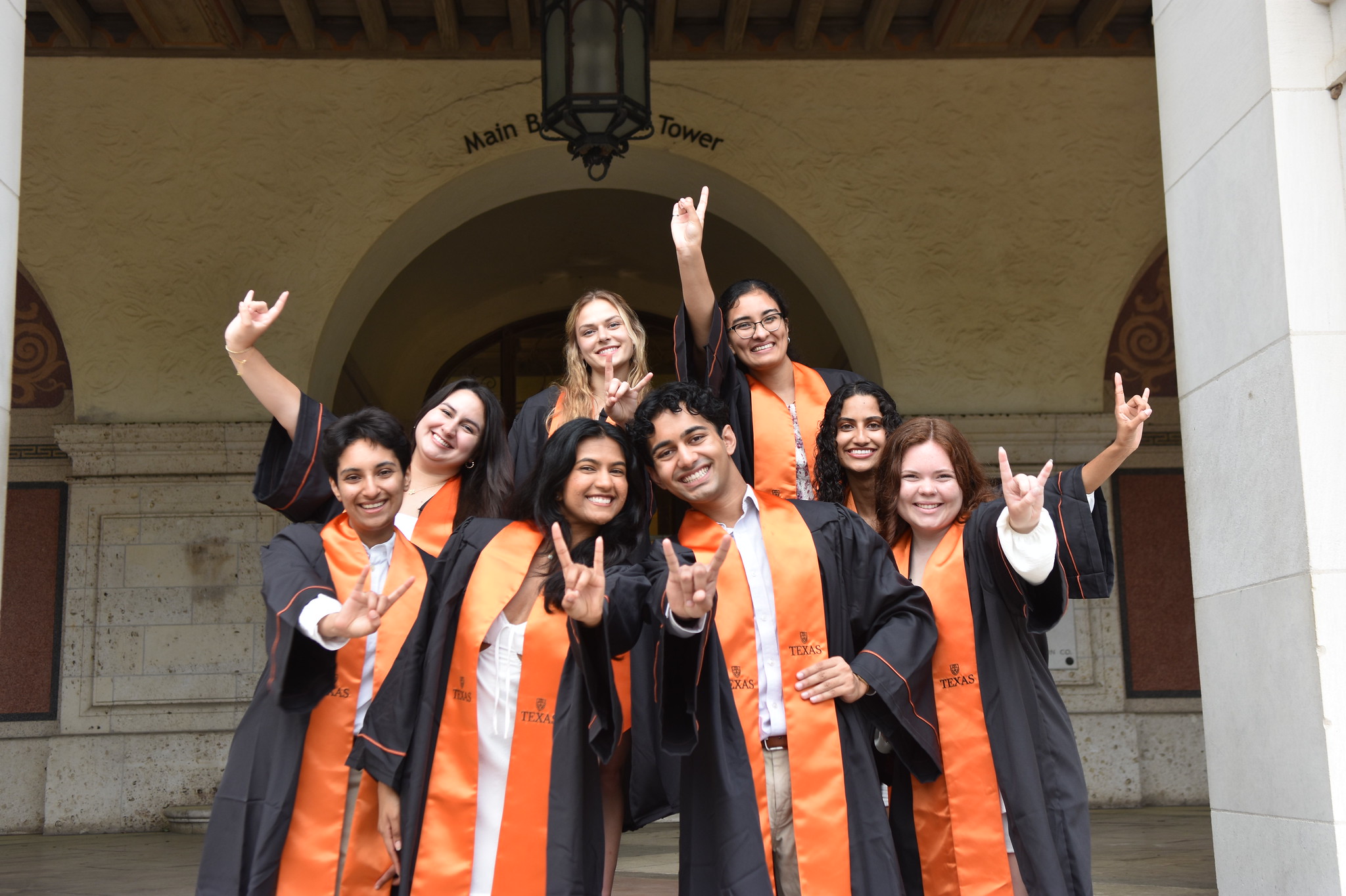 Graduating students smiling in cap and gown and posing in front of building on UT Austin campus.