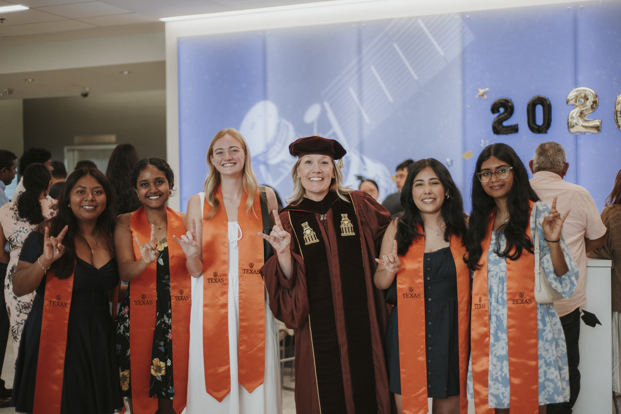 ASE/EM graduating students all smiling together with a professor while wearing graduation regalia.