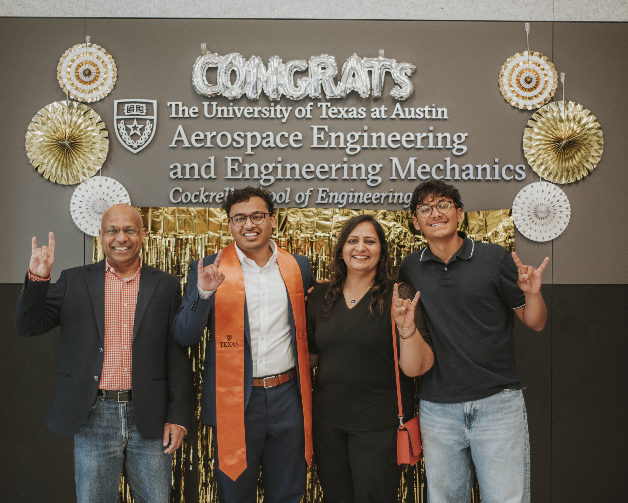 Texas Engineering student smiling with family while wearing graduation regalia under decorations.