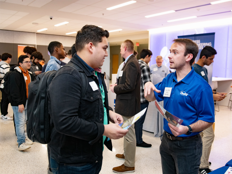 Student talking to industry representative in crowded room during Industry Open House event.