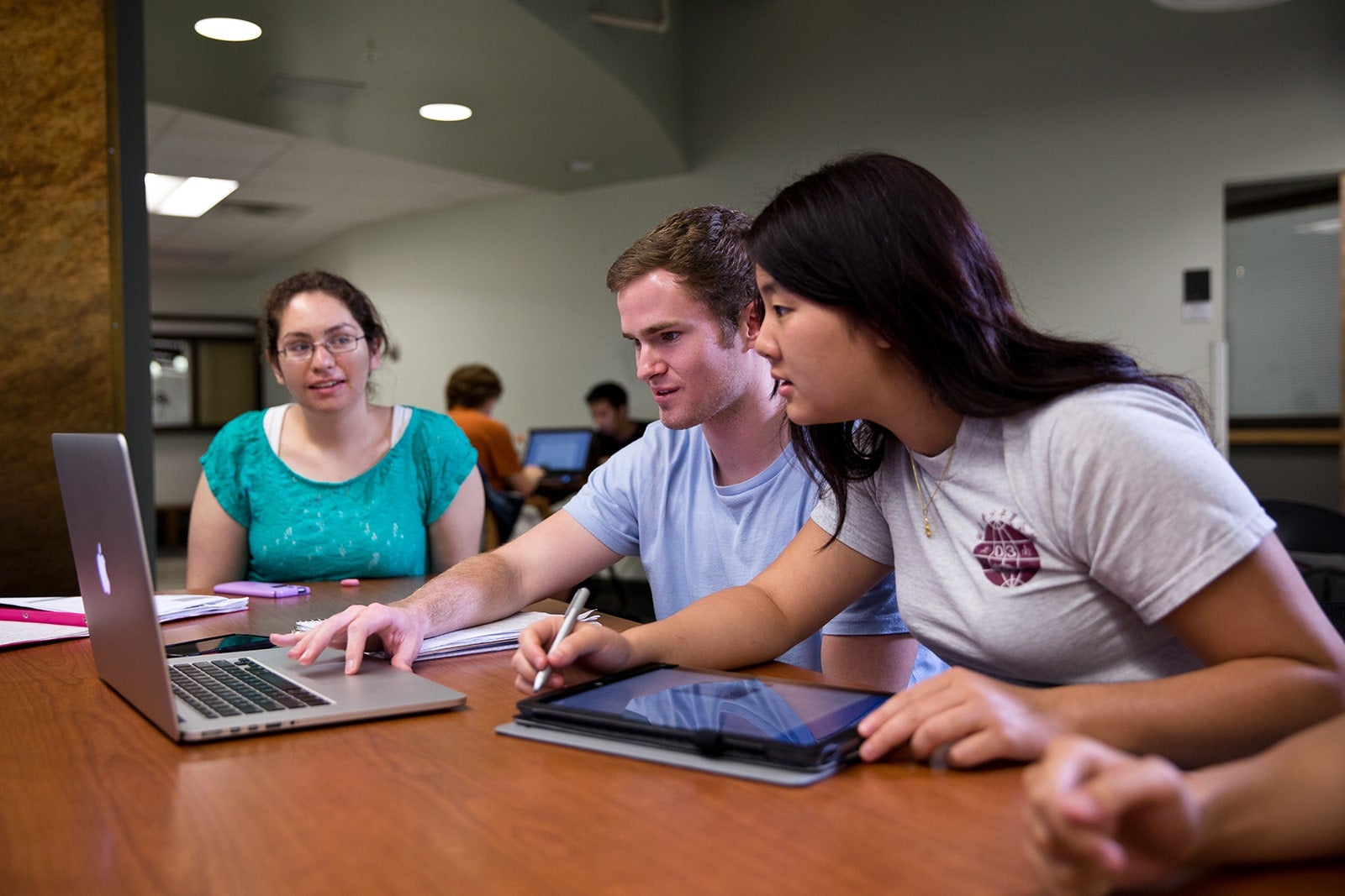 Students huddled around a laptop at a desk in common study space.