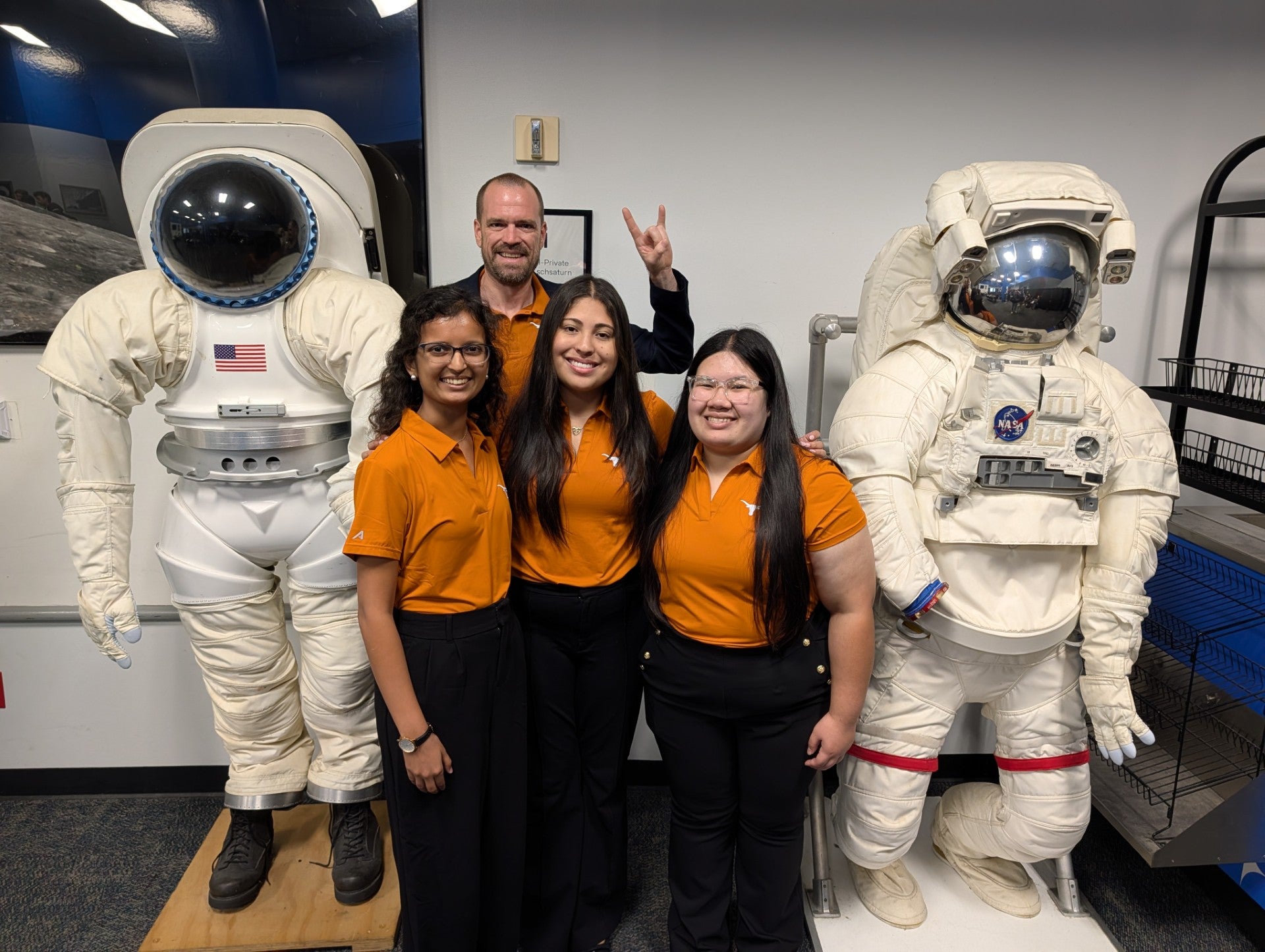 Students and Adam Nokes smiling next to astronaut suits