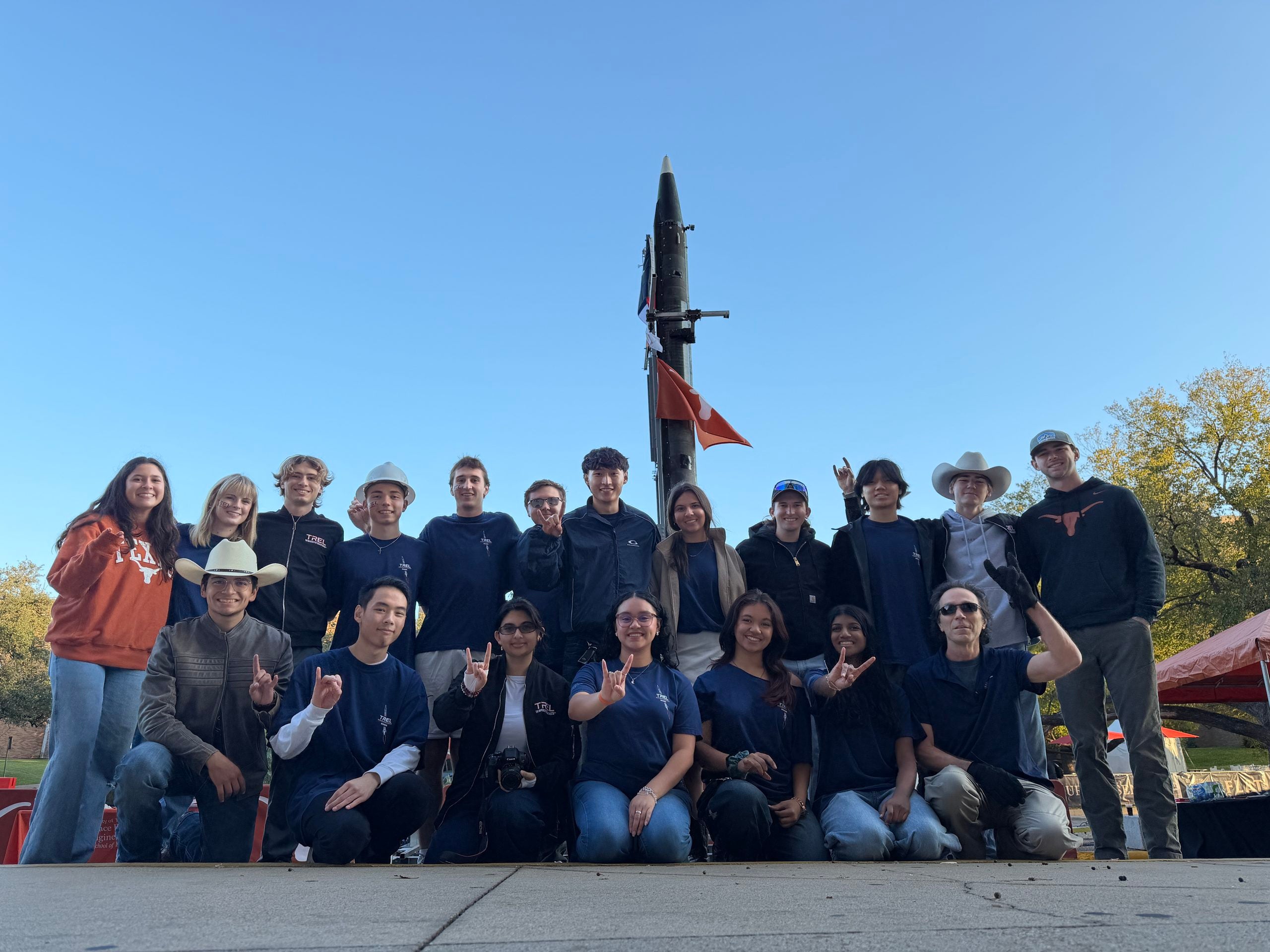 TREL students smiling and posing in front of rocket