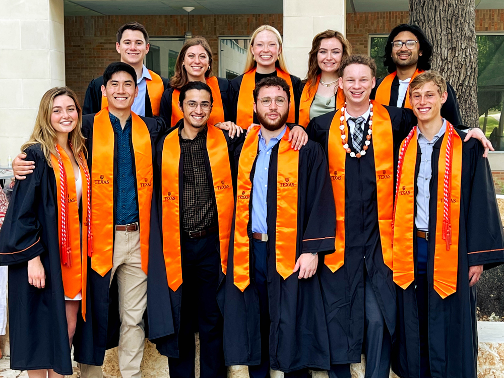 Group of Texas Engineering students wearing graduation regalia smiling together.
