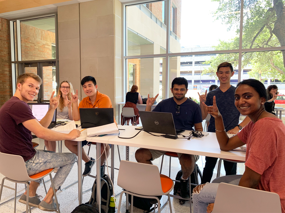 Students sitting around a table together with laptops and projects.
